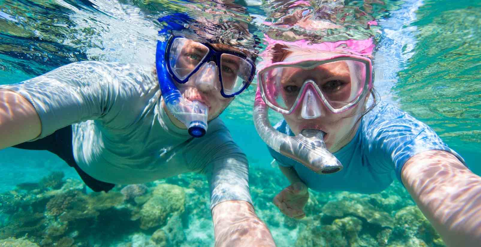 people snorkeling underwater looking at camera